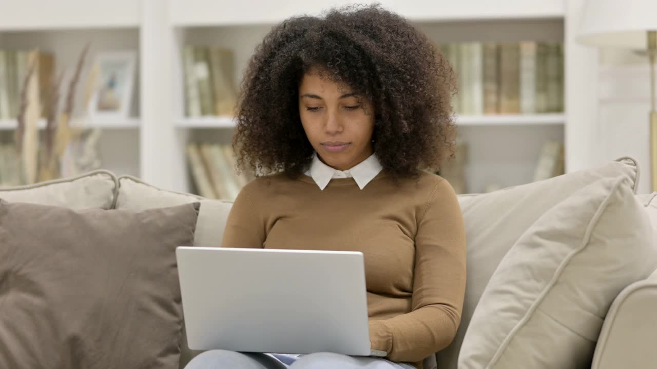 年轻的非洲妇女用笔记本电脑对沙发上的失败做出反应视频素材