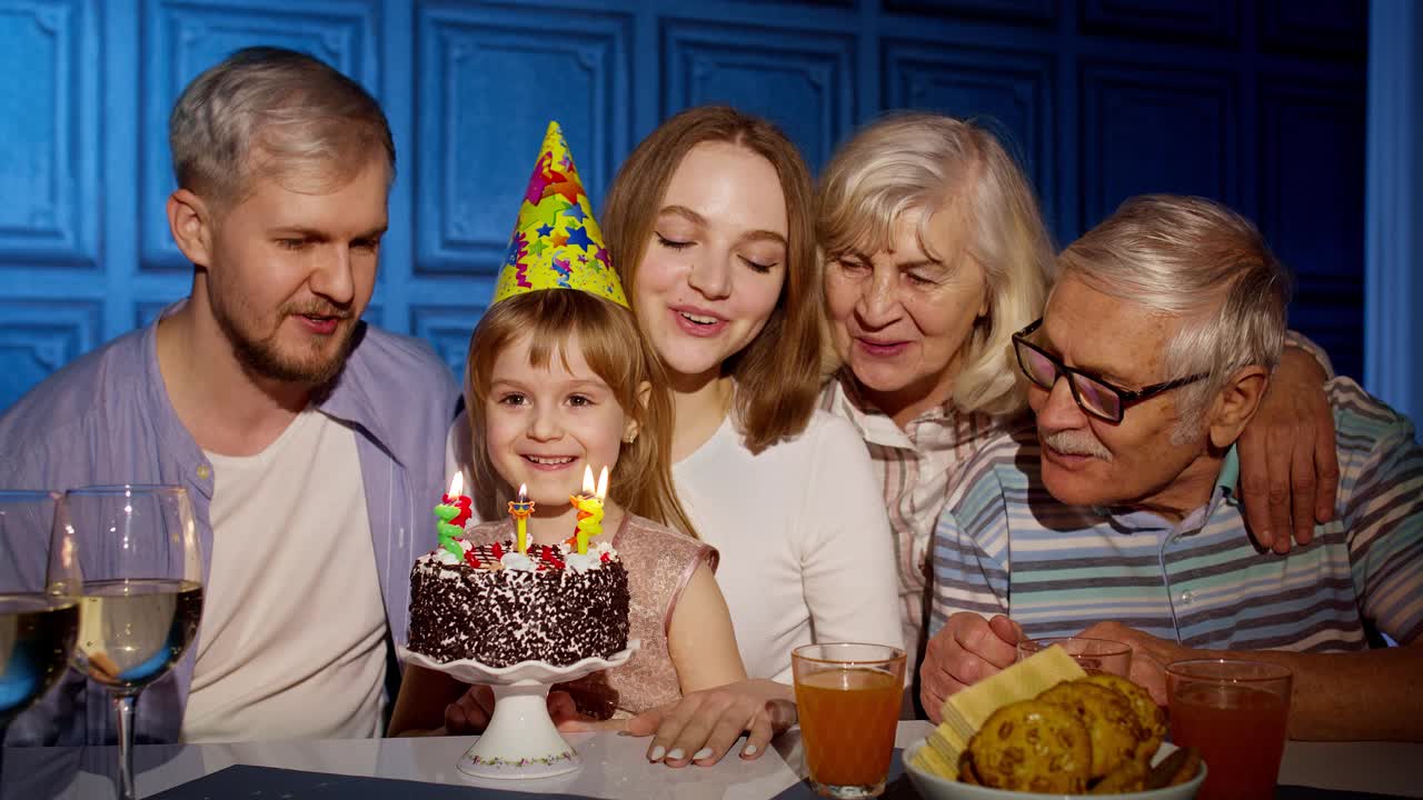 女孩和父母一起庆祝生日，爷爷奶奶家在蛋糕上吹蜡烛视频素材