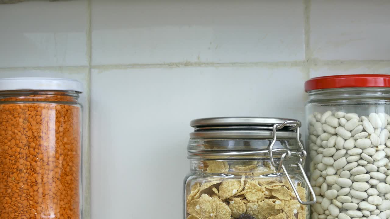 一名男子在厨房食品储藏室的架子上摆放着装满豆类的罐子。视频下载