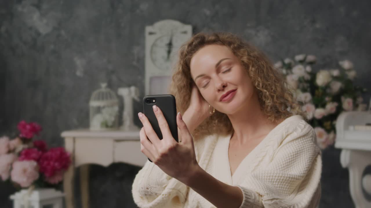 20多岁的年轻金发卷毛成年白人女性正看着智能手机的自拍照，就像在镜子里一样视频素材