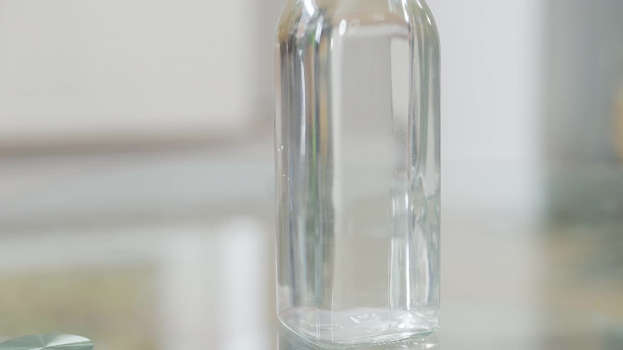 特写的女性白种人的手把空瓶子放在玻璃桌上。一个在室内喝酒的女人视频下载