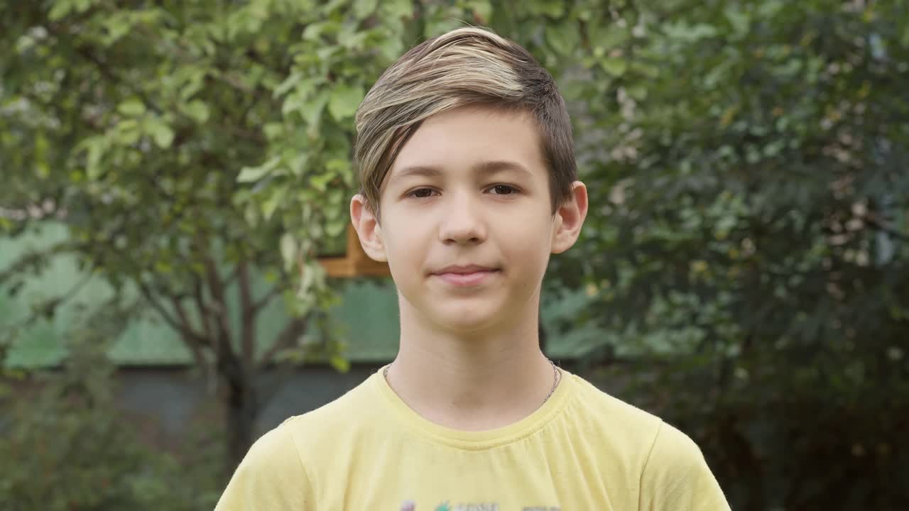 一个男孩的肖像与时尚的发型看着相机和微笑的户外视频下载