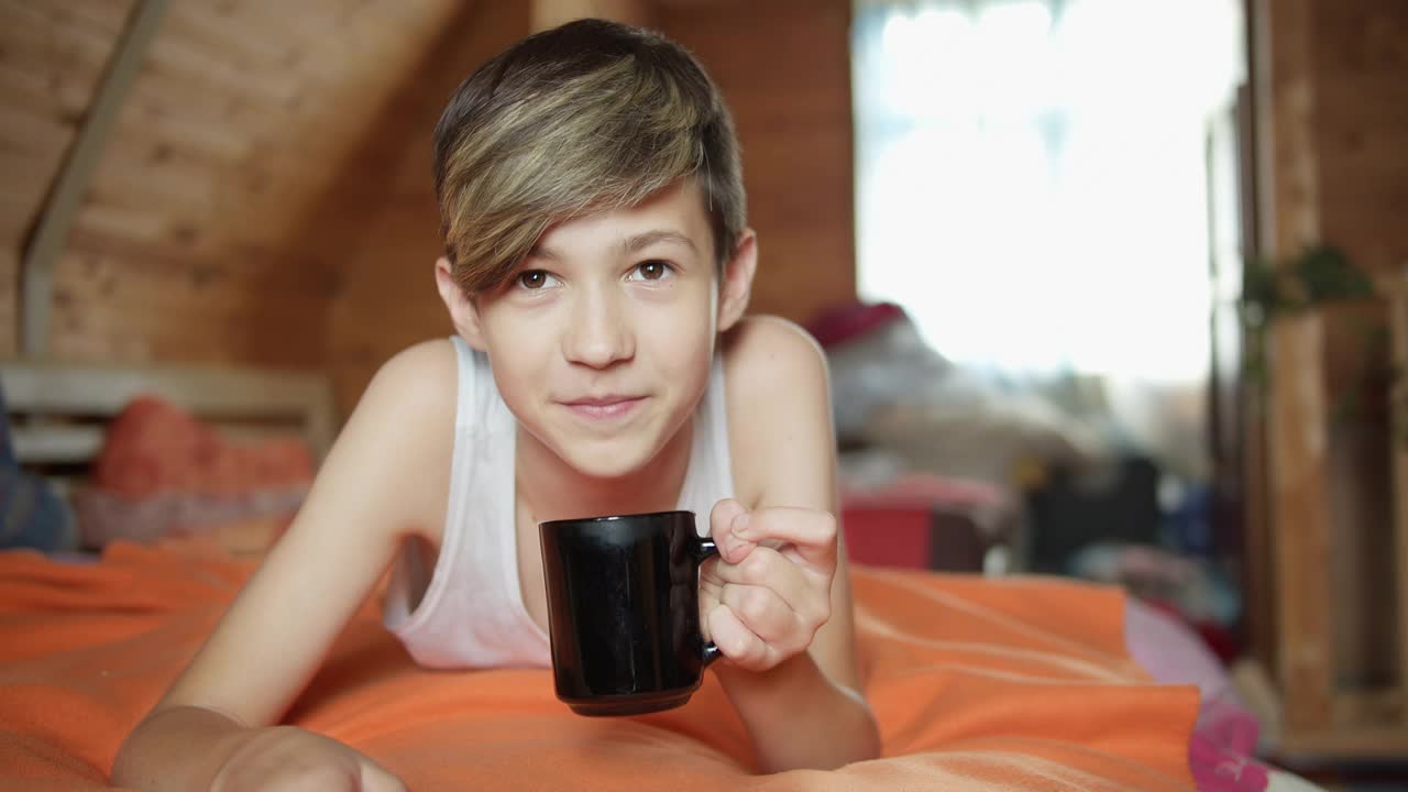 快乐的男孩躺在床上喝茶，兴致勃勃地看，乡村别墅，旅游视频下载