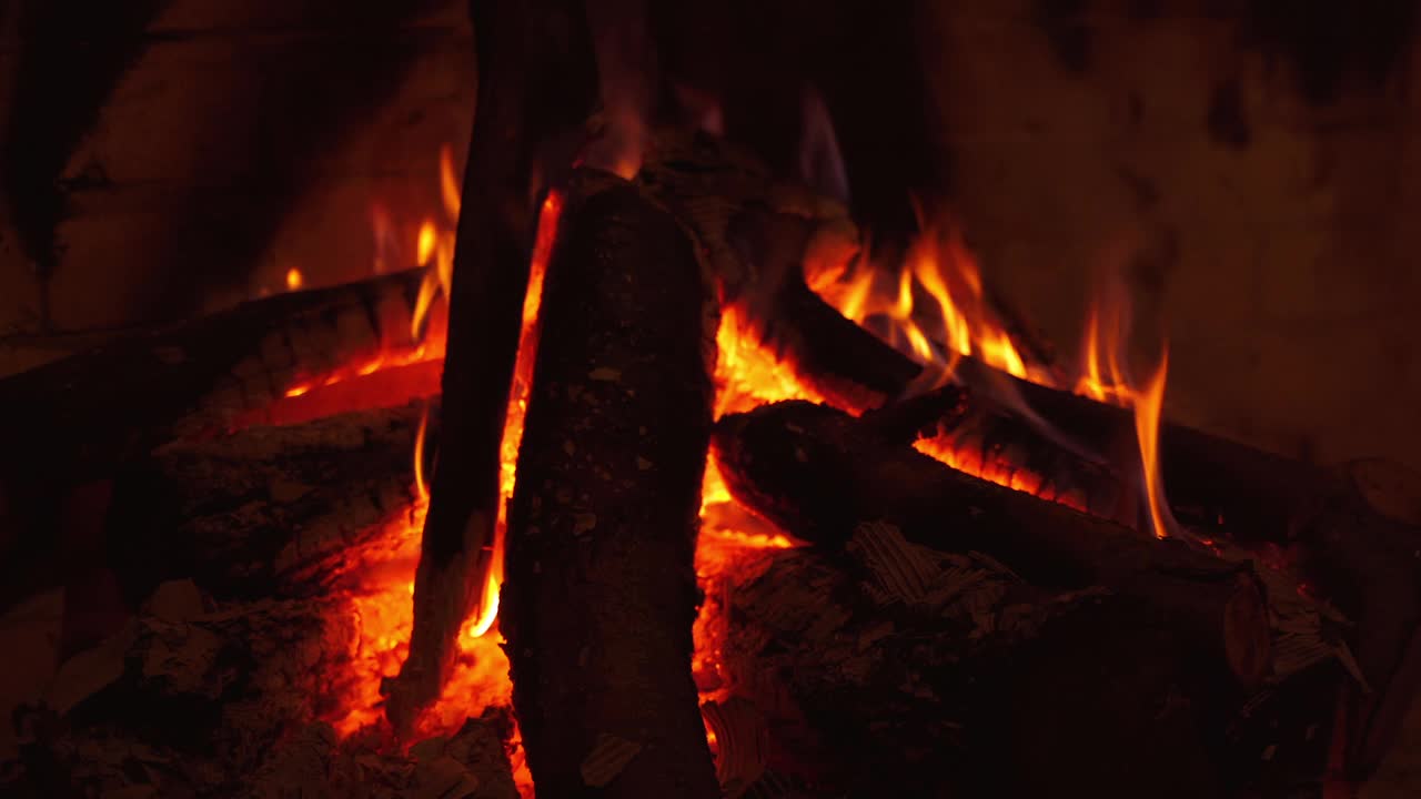 在壁炉里燃烧的木头发出炽热的火焰。舒适的黑暗背景与轻微的火在壁炉与原木在家里。特写镜头。视频素材