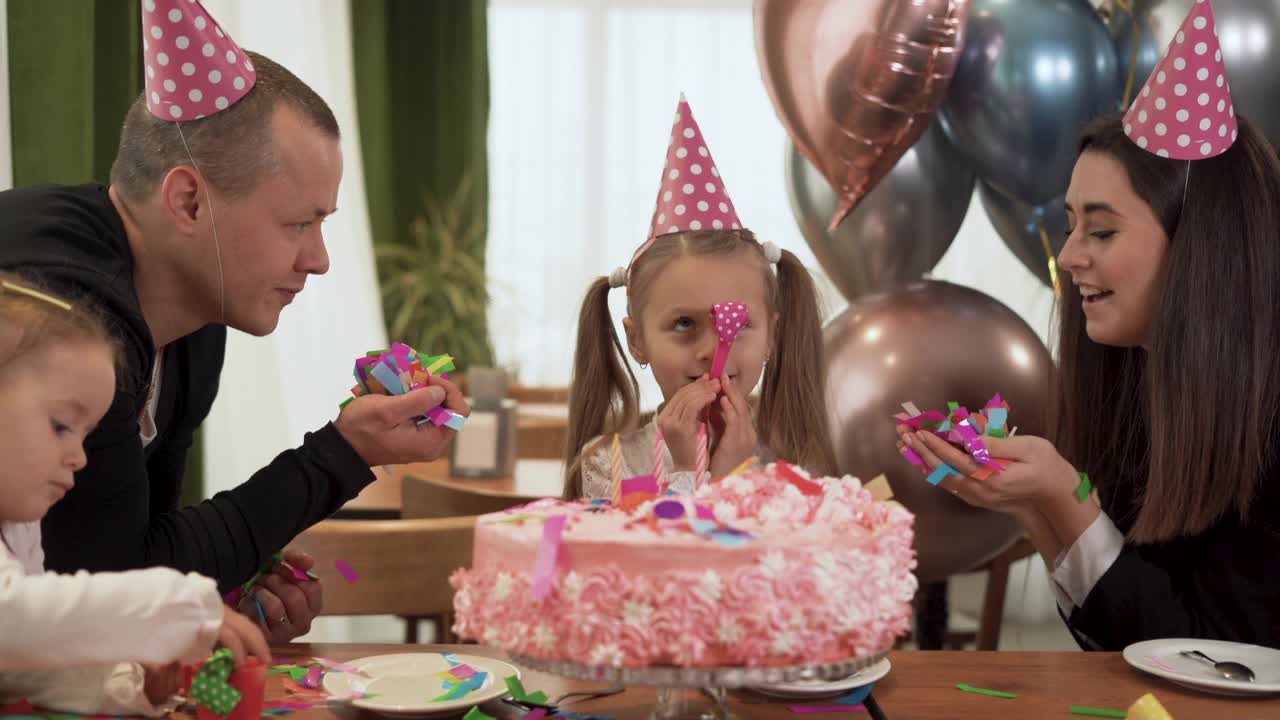 大家庭的爸爸，妈妈和两个女儿庆祝女孩的生日。父母向女儿撒五彩纸屑。视频素材