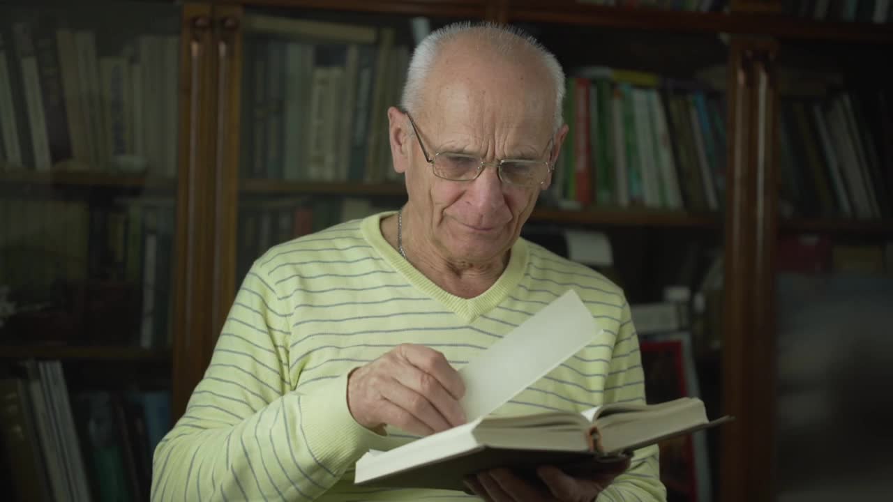 一位戴眼镜的老人手里拿着书签读圣经。视频素材