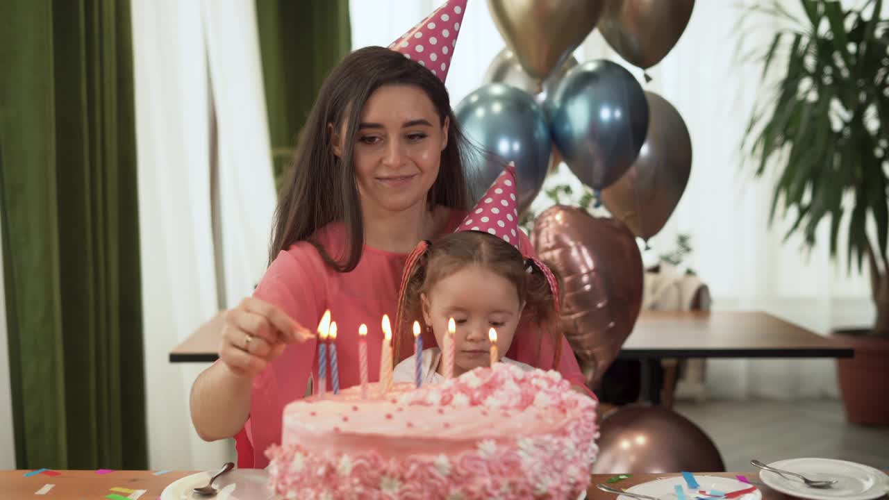 妈妈和女儿坐在家里的桌子旁庆祝他们的生日。一个女人用火柴点燃蜡烛。视频素材