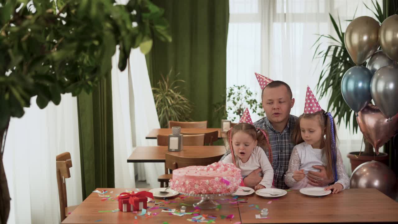 家人在家里过生日，爸爸和两个女儿正坐在桌旁。妈妈用一把锋利的刀切蛋糕。视频素材