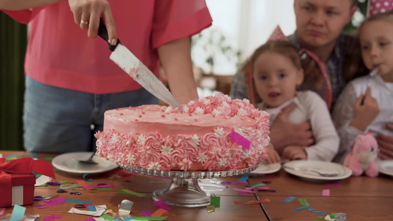 大家庭的爸爸，妈妈和两个女儿在家里庆祝女孩的生日。坐在家里的桌子旁，一个女人正在切生日蛋糕。视频素材