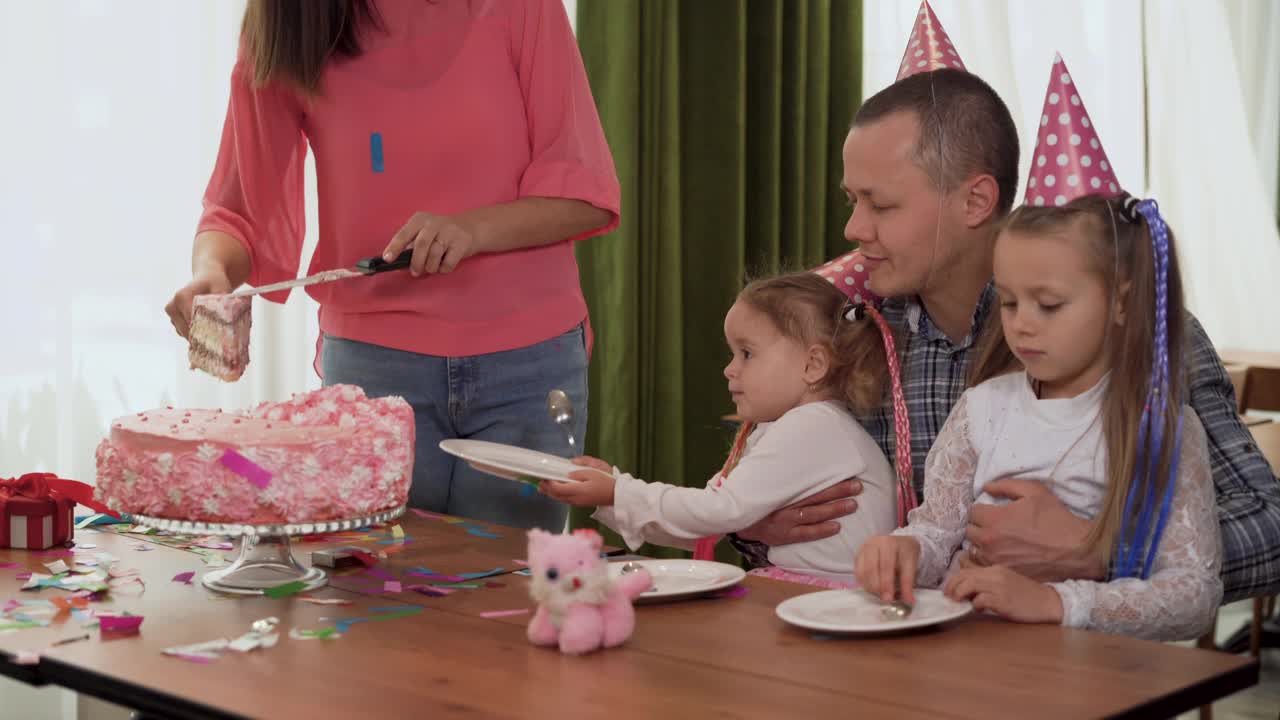 欢乐的家庭聚会。快乐的父母和孩子在室内庆祝他们的生日。女儿端上盘子，母亲放上蛋糕。视频素材