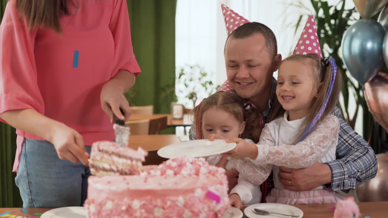 欢乐的家庭聚会。快乐的父母和孩子在室内庆祝他们的生日。女儿端上盘子，母亲放上蛋糕。视频素材