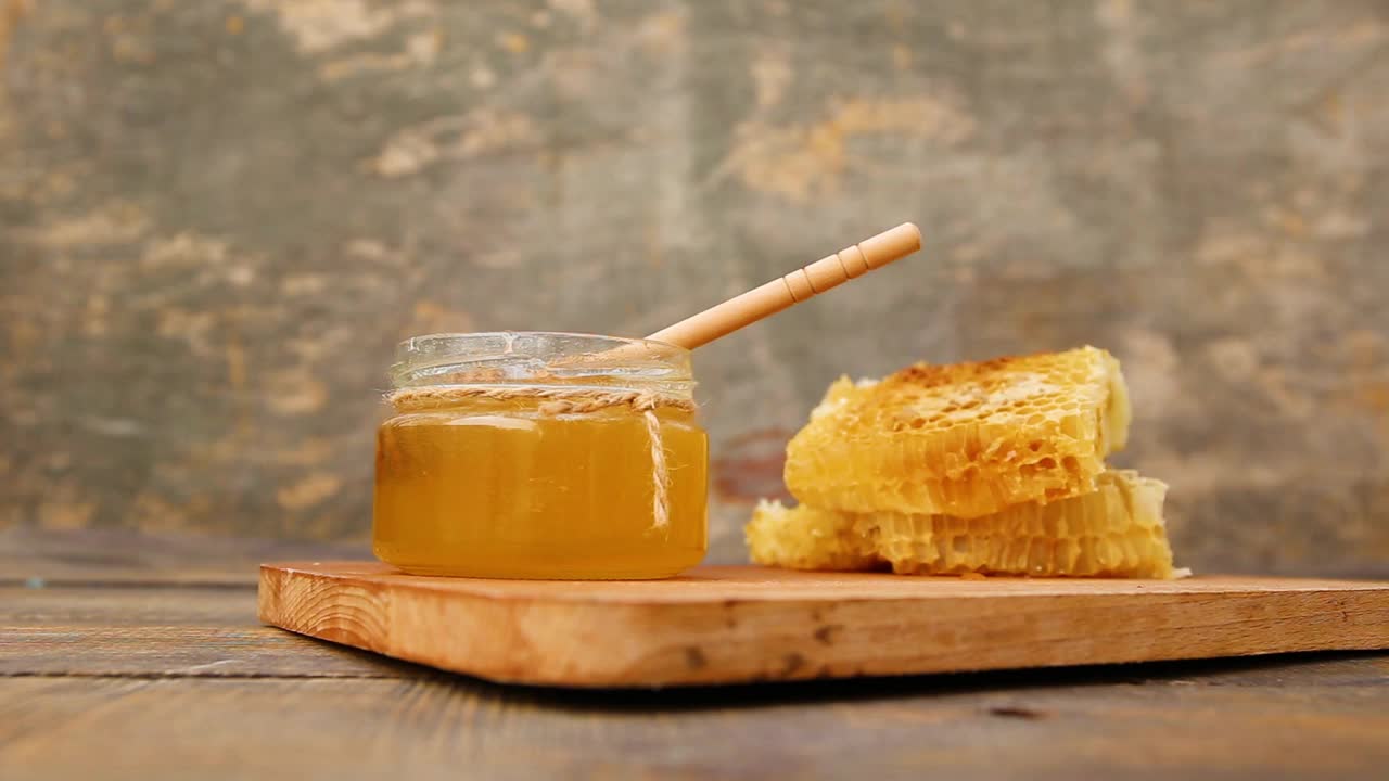 蜂蜜在一个罐子和蜂巢在一个古老的木制背景。视频素材