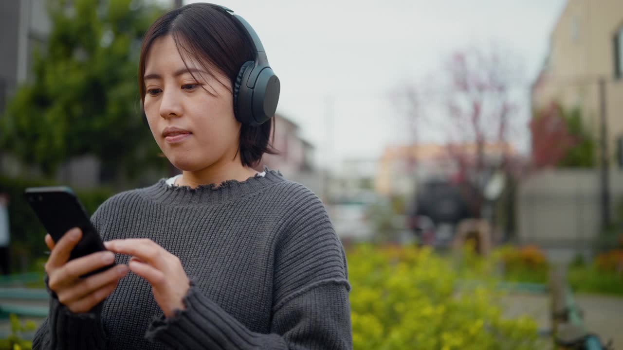 年轻女子在公园边听音乐边用智能手机视频下载