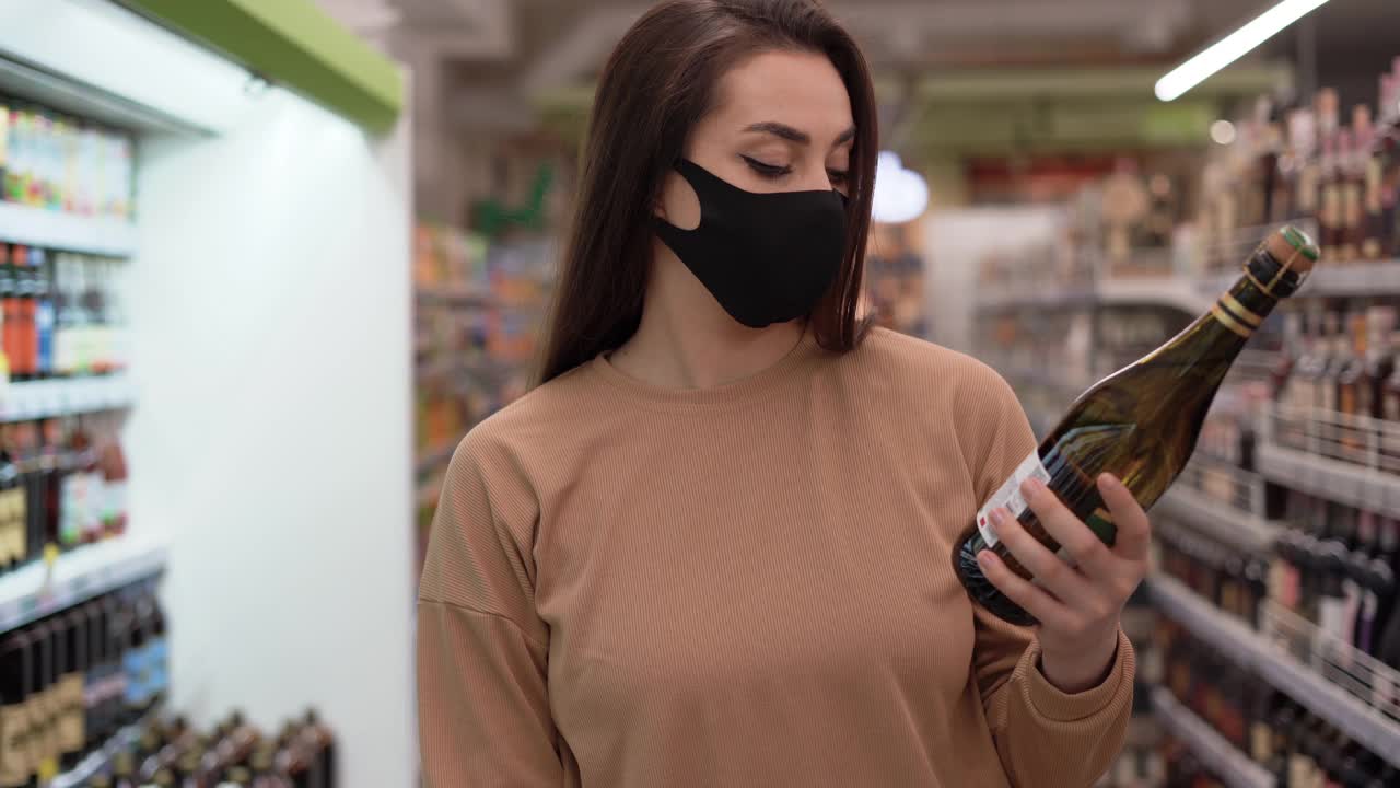 戴着防护面具的女人在超市挑选葡萄酒。隔离期间的日常生活。冠状病毒疾病的医疗和预防。视频素材