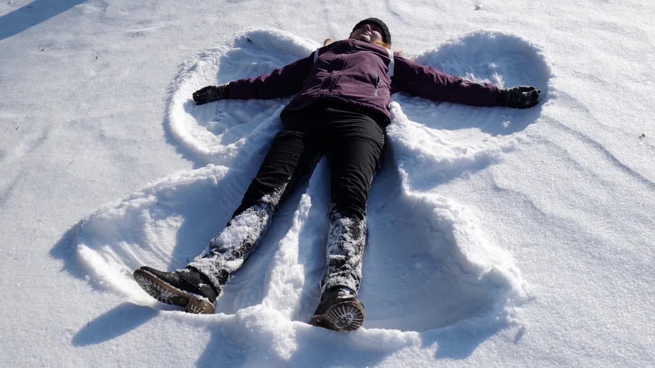 女孩躺在雪地里做了一个雪天使。女孩在雪中快乐视频下载
