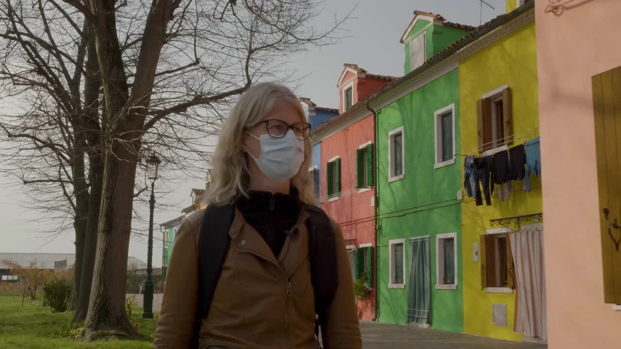 一位中年妇女戴着保护面罩经过布拉诺色彩斑斓的房屋视频下载