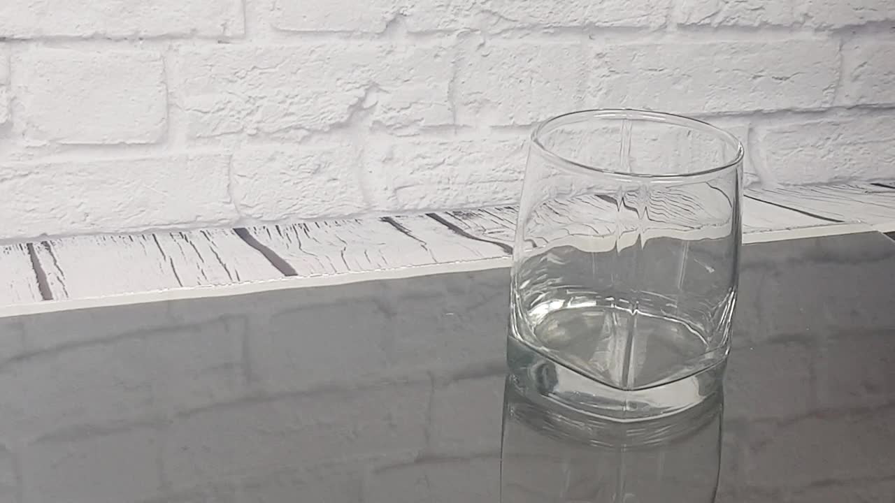将新鲜牛奶倒入透明的玻璃杯中，对着白砖墙，这就是乳制品的概念。往杯子里倒牛奶特写，4K视频视频素材
