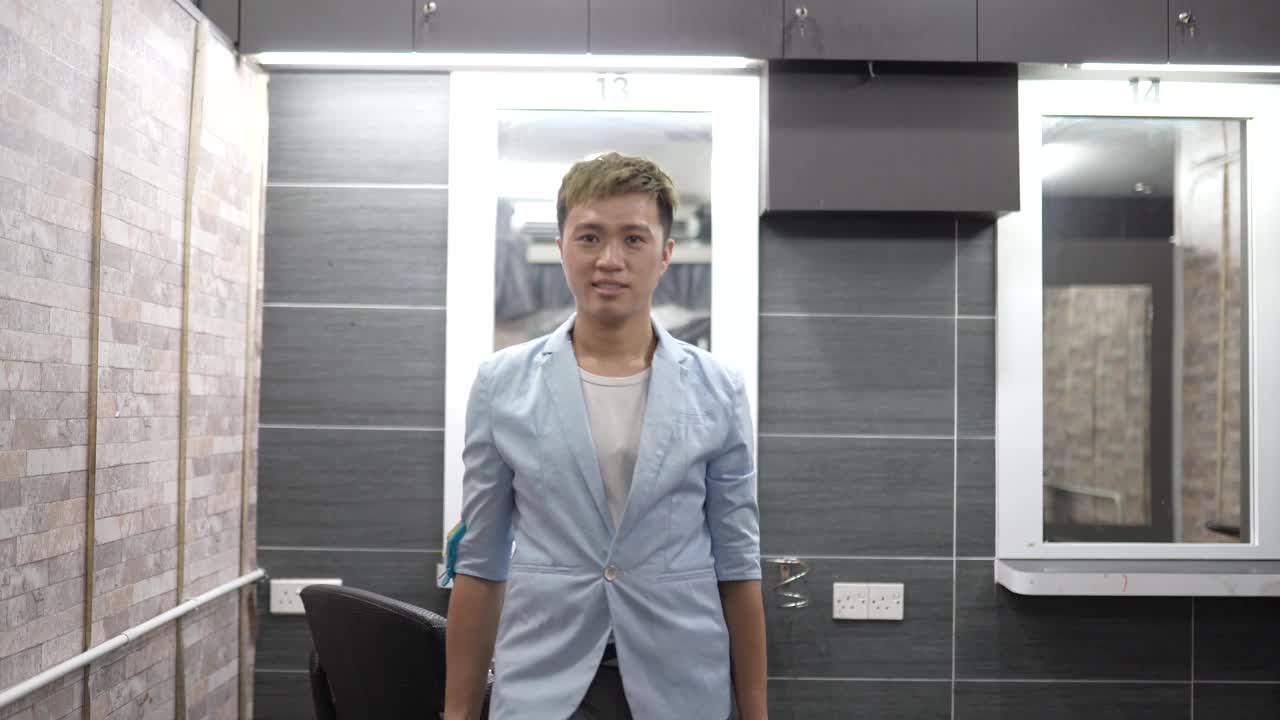 亚洲华人男性美发师在他的沙龙里对着镜头微笑。理发店。视频下载