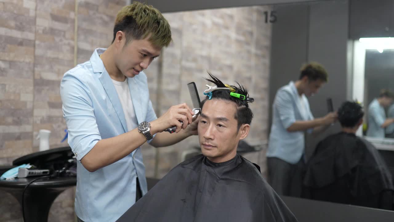 亚洲华人男性理发师在美发厅用理发剪为男士理发。理发店。视频素材