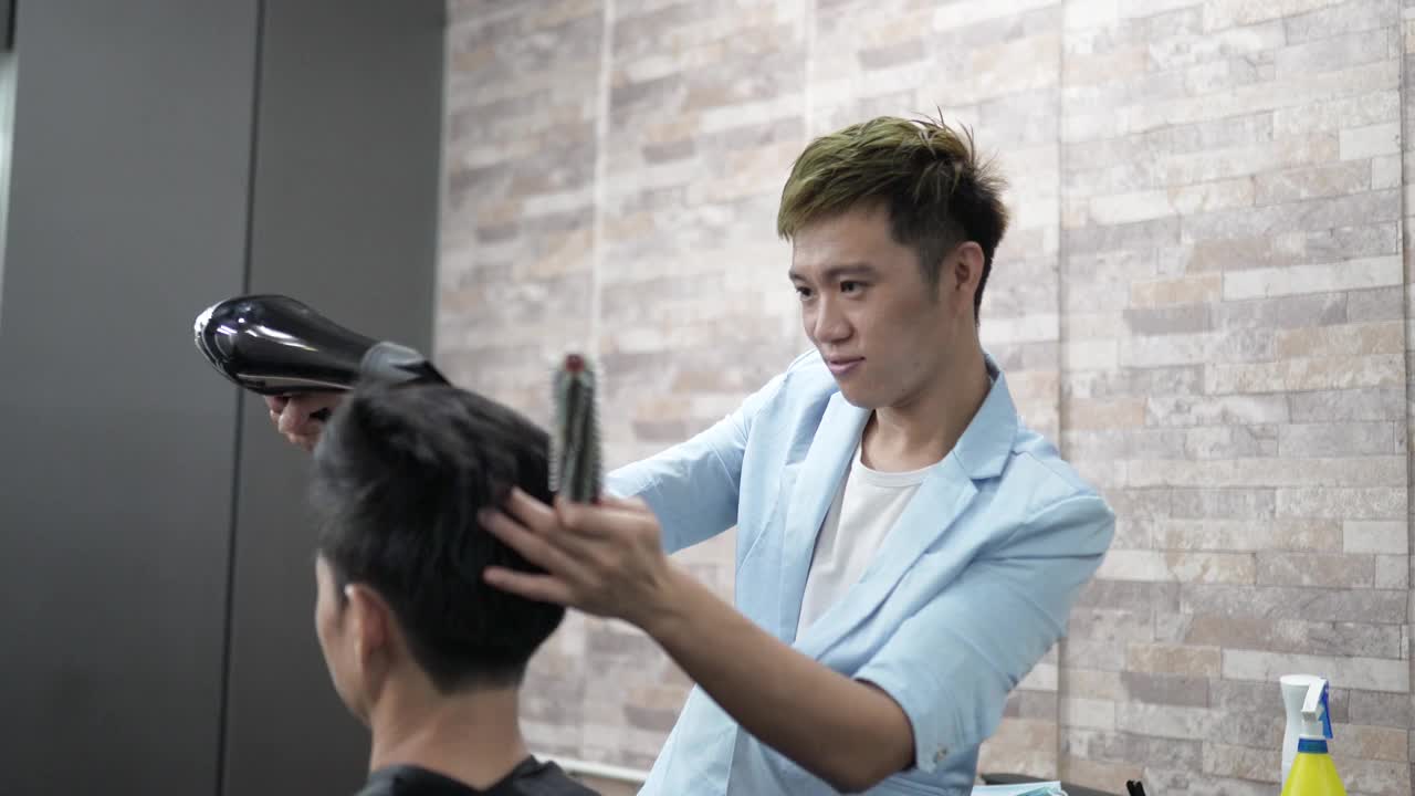 亚洲华人理发师，在他的沙龙里干燥和造型男人的头发。视频下载