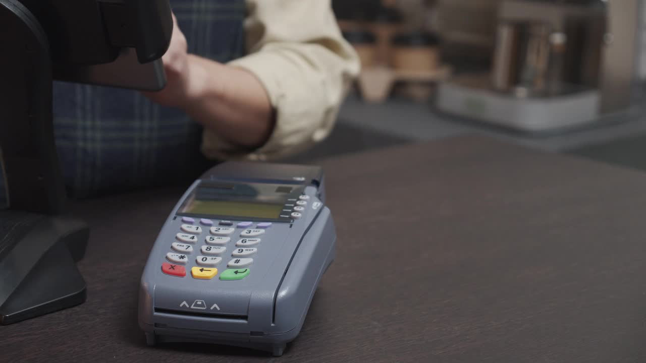 顾客使用带有NFC技术的智能手机进行非接触式支付，在咖啡馆餐厅使用信用卡读卡机的咖啡师在吧台，无现金的技术概念。视频素材