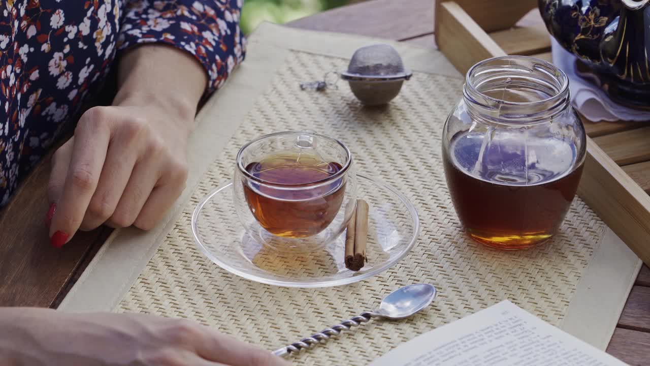近距离观察年轻女子的手倒蜂蜜天然甜味剂热茶杯在一张桌子上的户外露台视频素材
