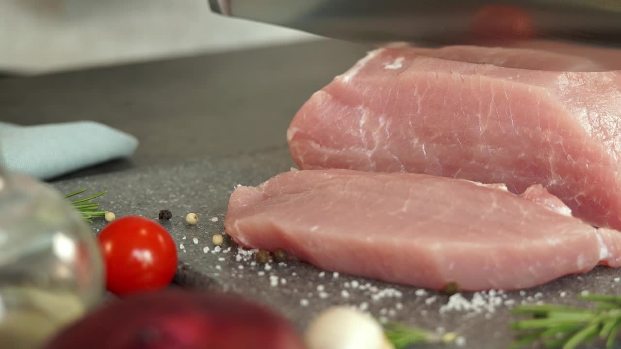 厨师用男性的手在蔬菜的背景上用刀切新鲜的猪肉。美食概念，烹饪肉排，里脊，碳酸。视频下载
