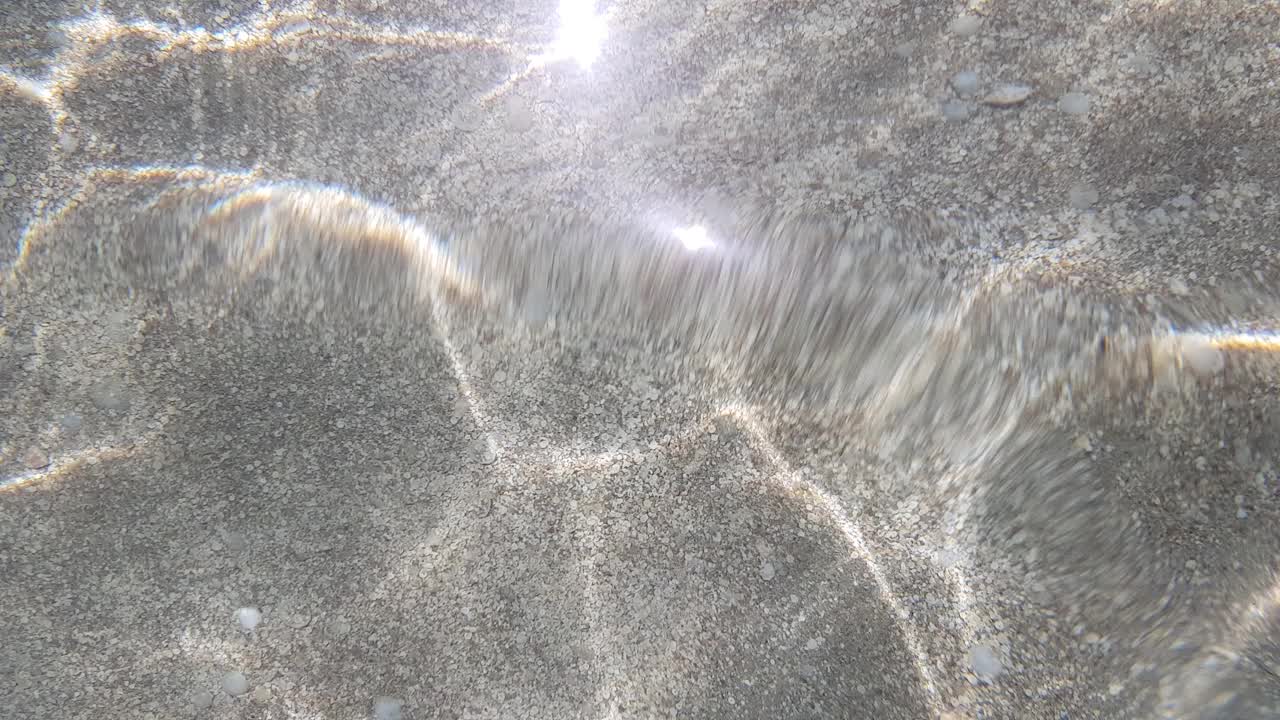 平静的海面上闪耀着太阳的光芒。透过清澈的水，可以看到底部的细砂砾。视频素材