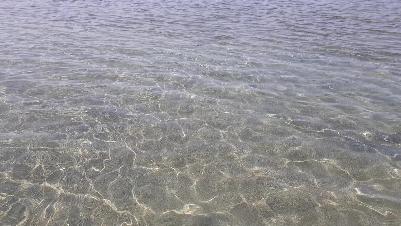 平静的海面上闪耀着太阳的光芒。透过清澈的水，可以看到底部的细砂砾。视频素材