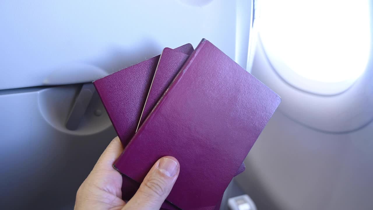 一个人(男子)在飞行时在飞机窗户旁边持有三本护照视频下载