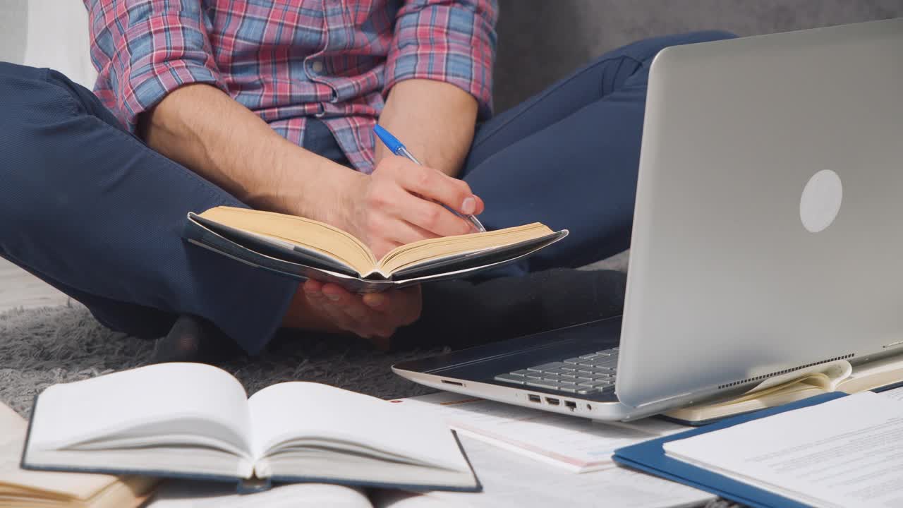一个面目全非的年轻人在网上学习，或者坐在家里的地板上用笔记本电脑和书做作业视频素材