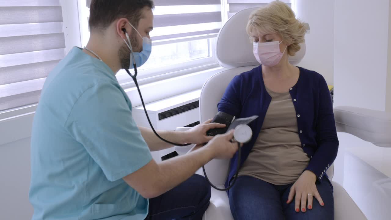 医生戴上防护口罩，用测量仪测量女患者的血压视频素材