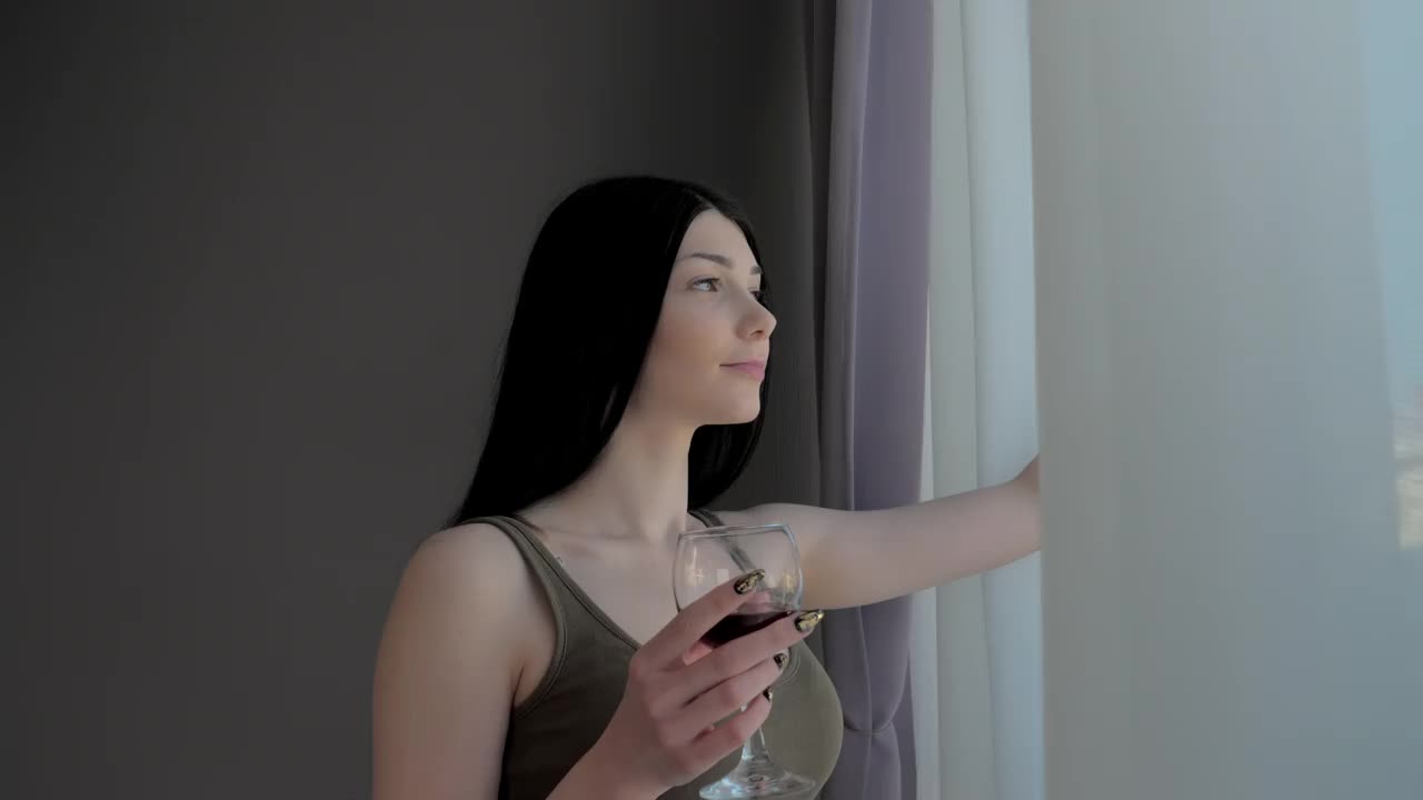 一个迷人的年轻女孩正在喝着葡萄酒，看着窗外视频下载