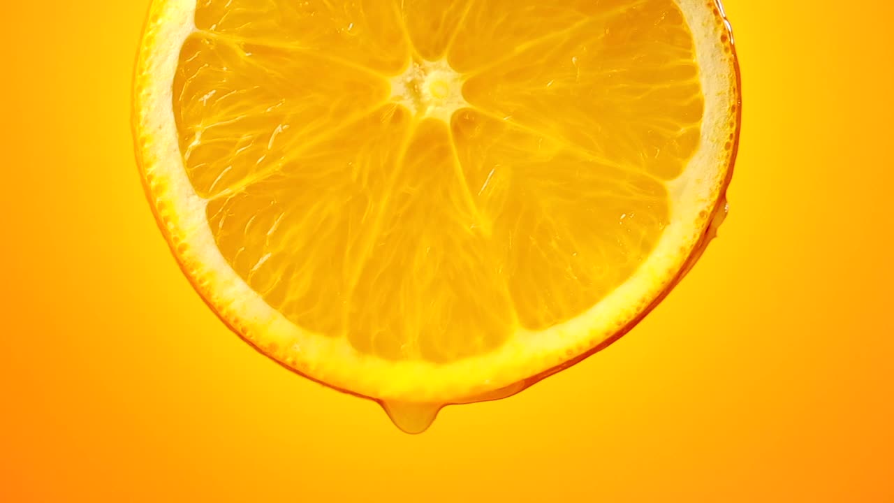 鲜榨橙汁滴从成熟的水果片近距离橘黄色背景慢动作视频素材