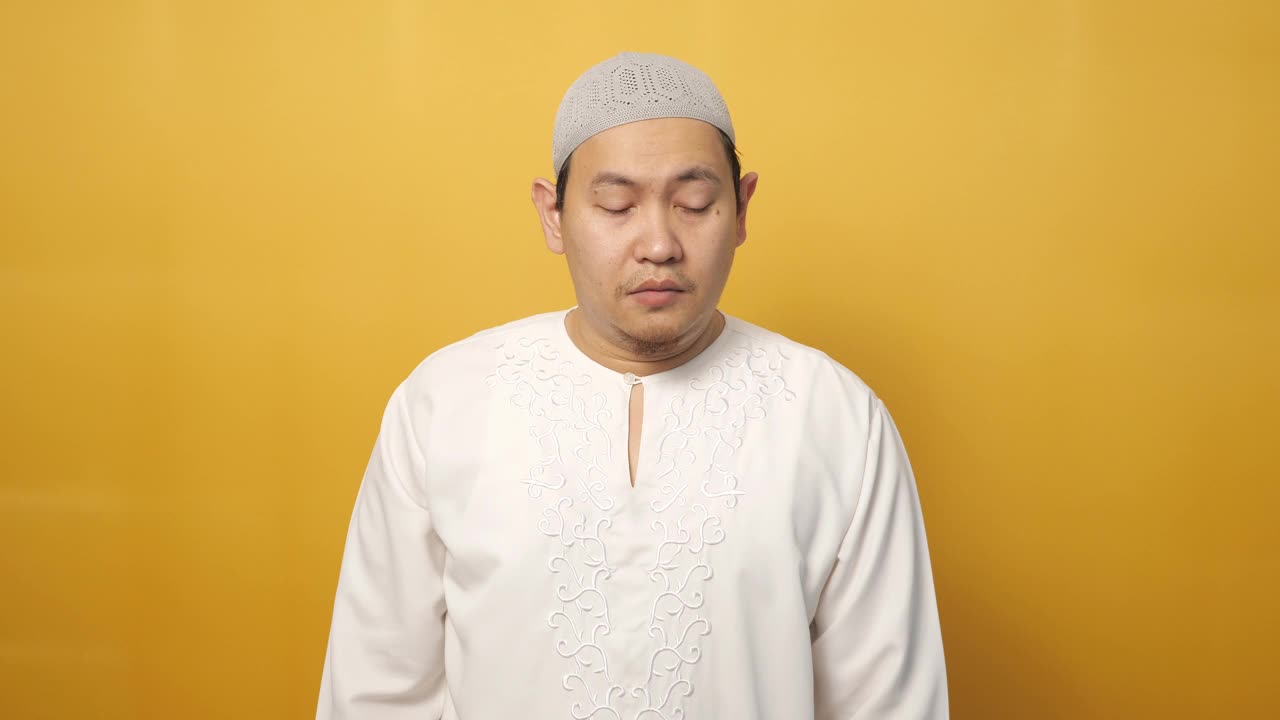 一幅亚洲穆斯林男子的肖像，在黄色背景下咬着指甲，看上去很担心，害怕发生什么不好的事情视频素材