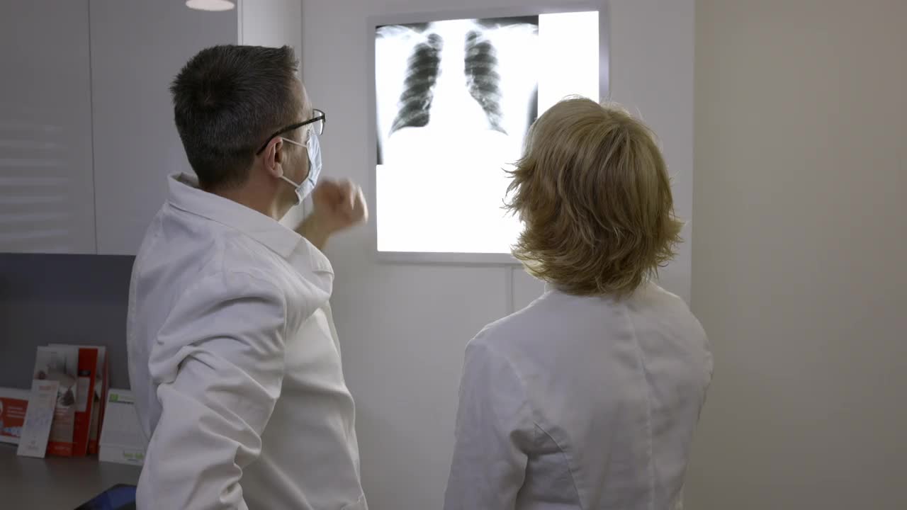 放射科医生戴着防护面罩，在阴性镜上观察x光的后视图视频素材