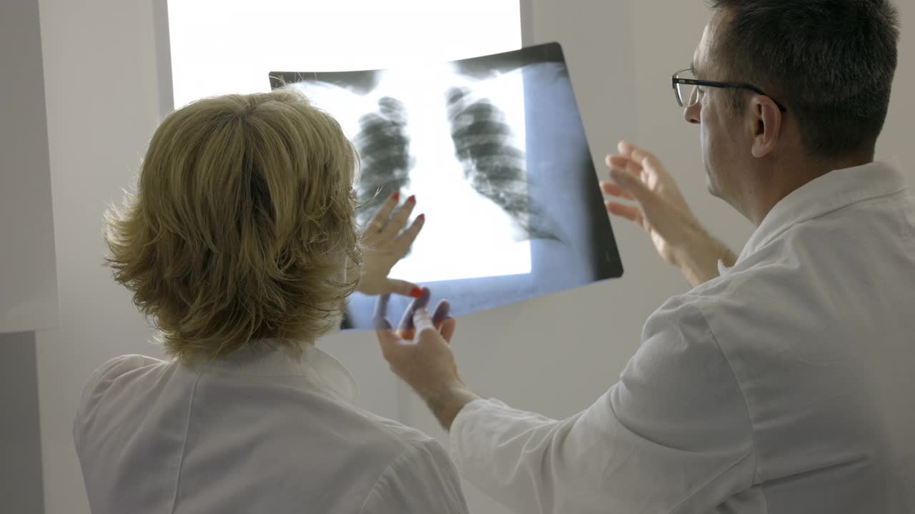 女医生和她的同事在阴性镜上检查x射线的后视图视频素材