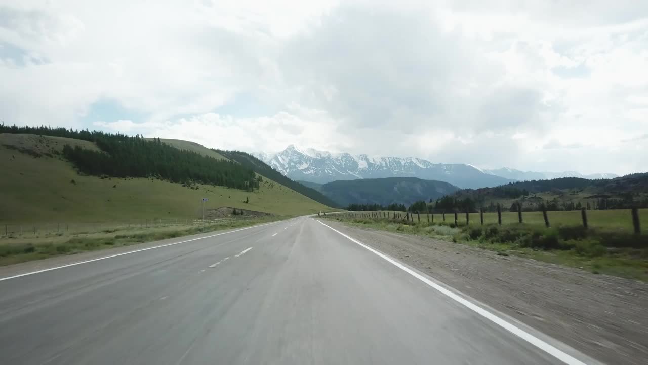 山开车。现场。POV从司机的视角穿过蜿蜒的山路，可以看到前面美丽的雪山山峰。加速视频。视频下载