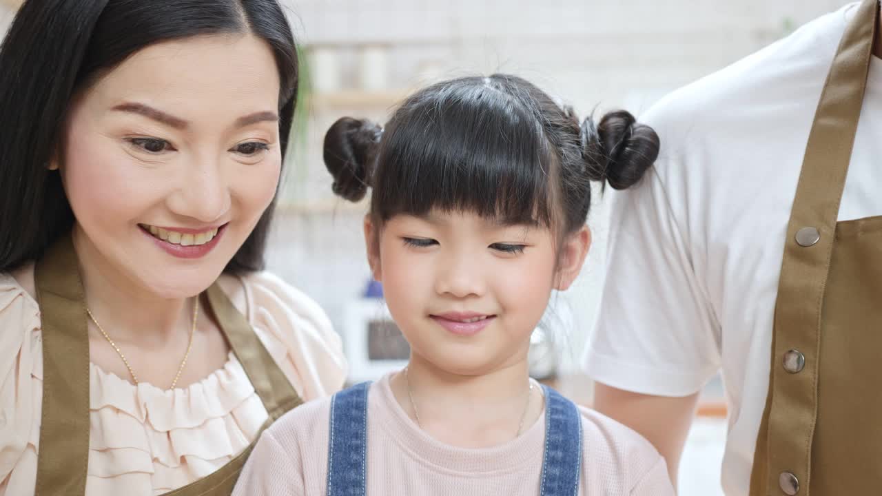 一个幸福的亚洲家庭在厨房里一起喝牛奶。小女孩和爸爸妈妈微笑着，互相看着对方，享受着在家里度过的时光。视频素材