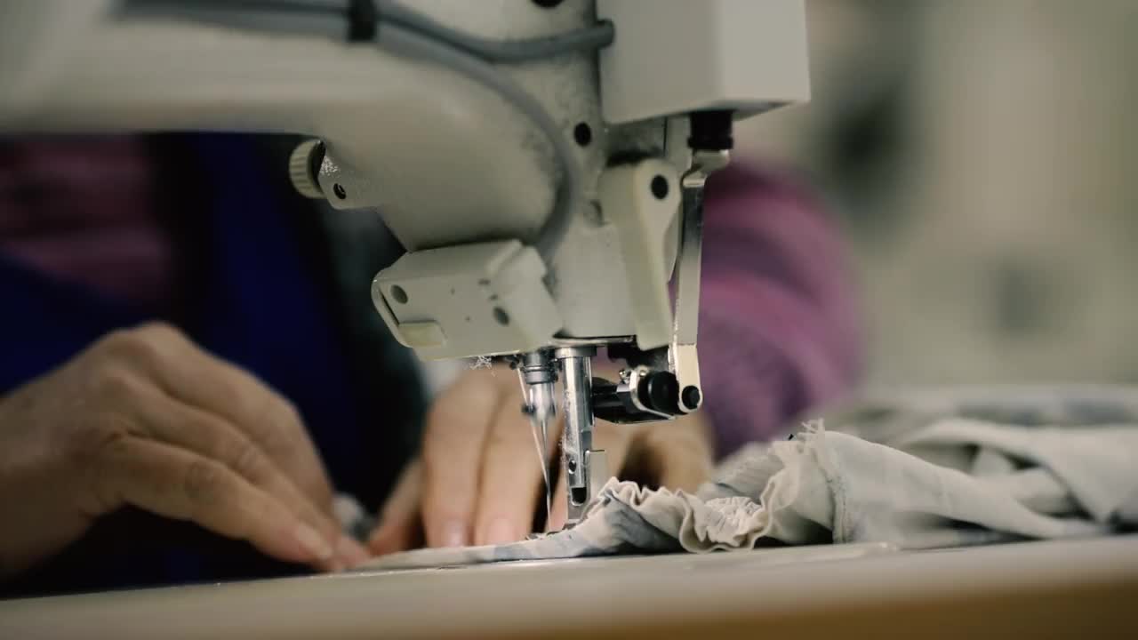 浅景深(选择性聚焦)镜头，一位在纺织厂电动缝纫机上工作的高级妇女的双手。视频素材