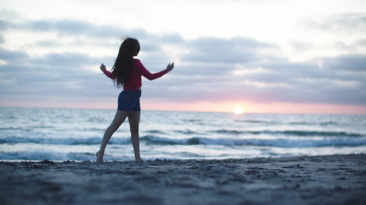 日落时分，年轻女子在海滩上跳舞视频素材