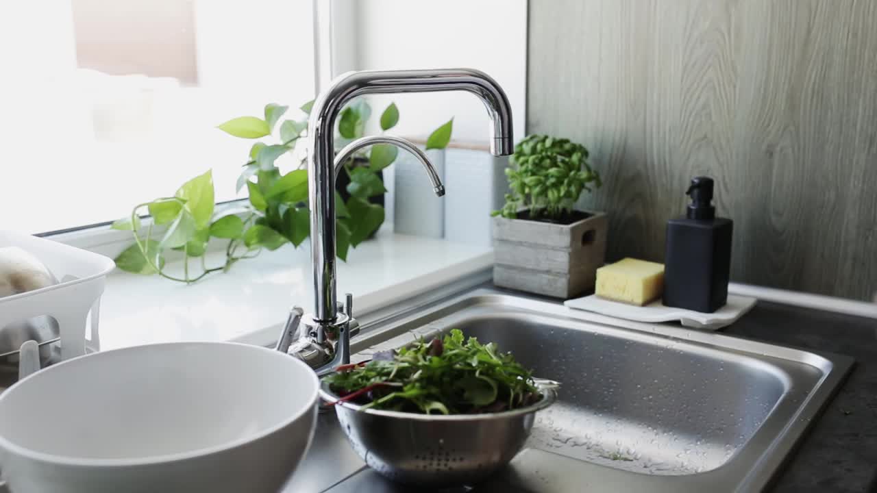 一名妇女在厨房水槽里用流动的水清洗生菜沙拉叶子视频下载