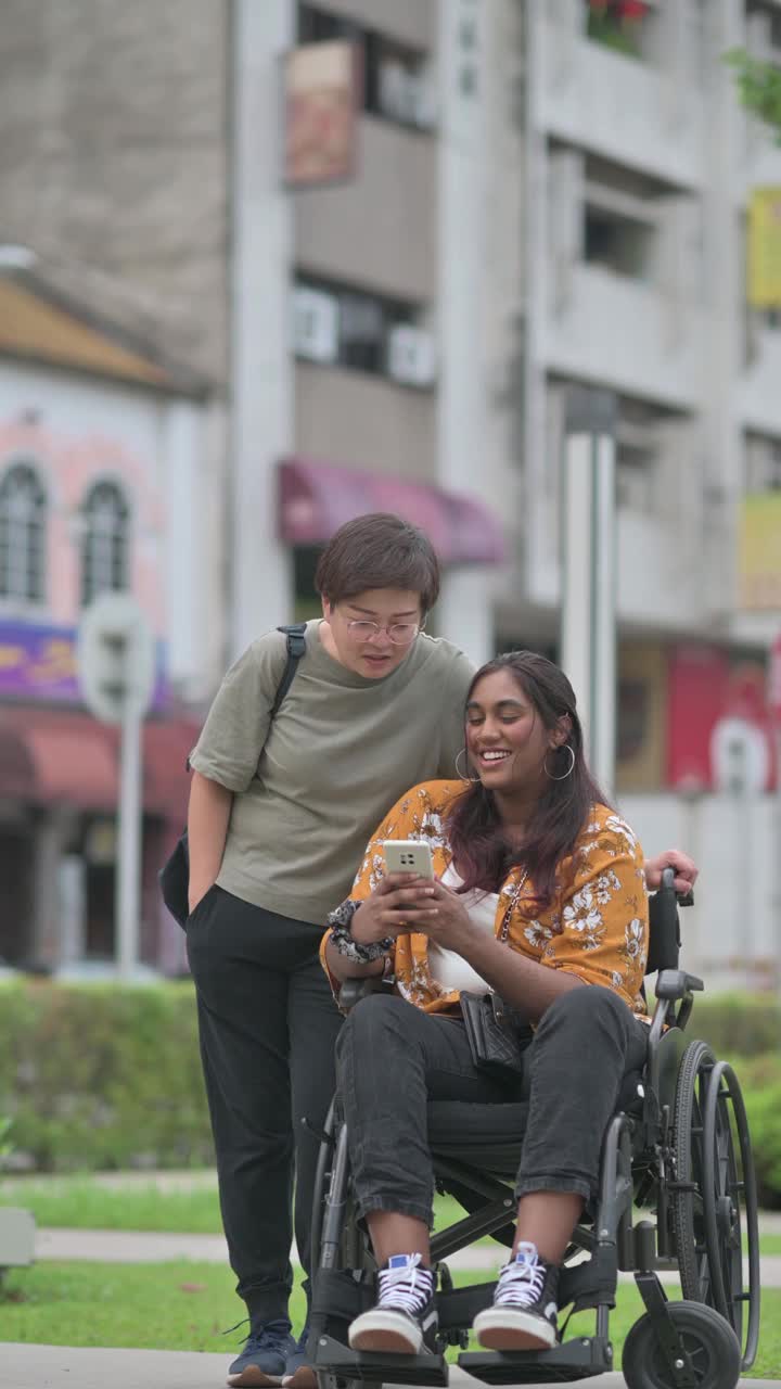 亚洲印度女性和她的女性朋友看智能手机在城市街道的人行道上视频下载