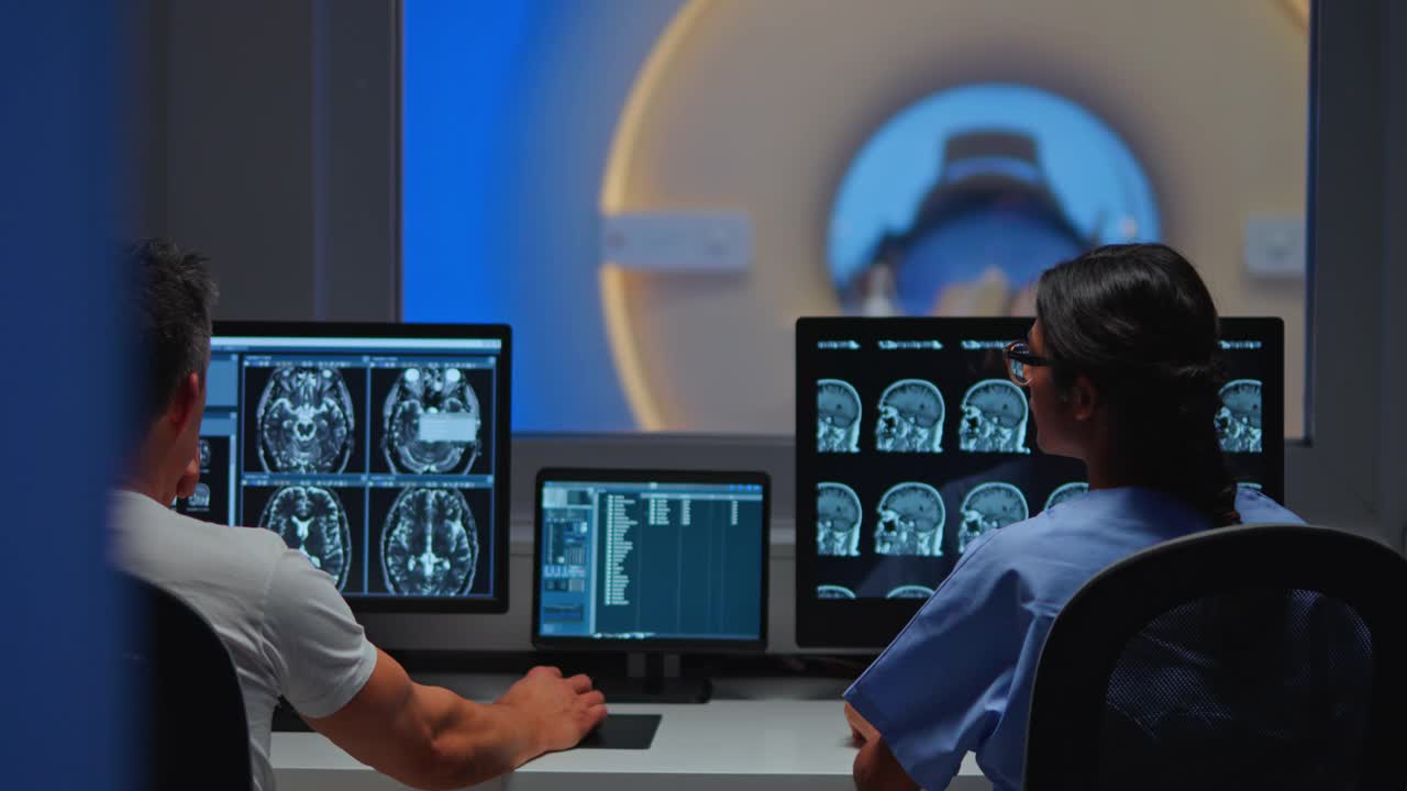 两名放射科医生在控制室看着电脑屏幕上的核磁共振图像视频素材