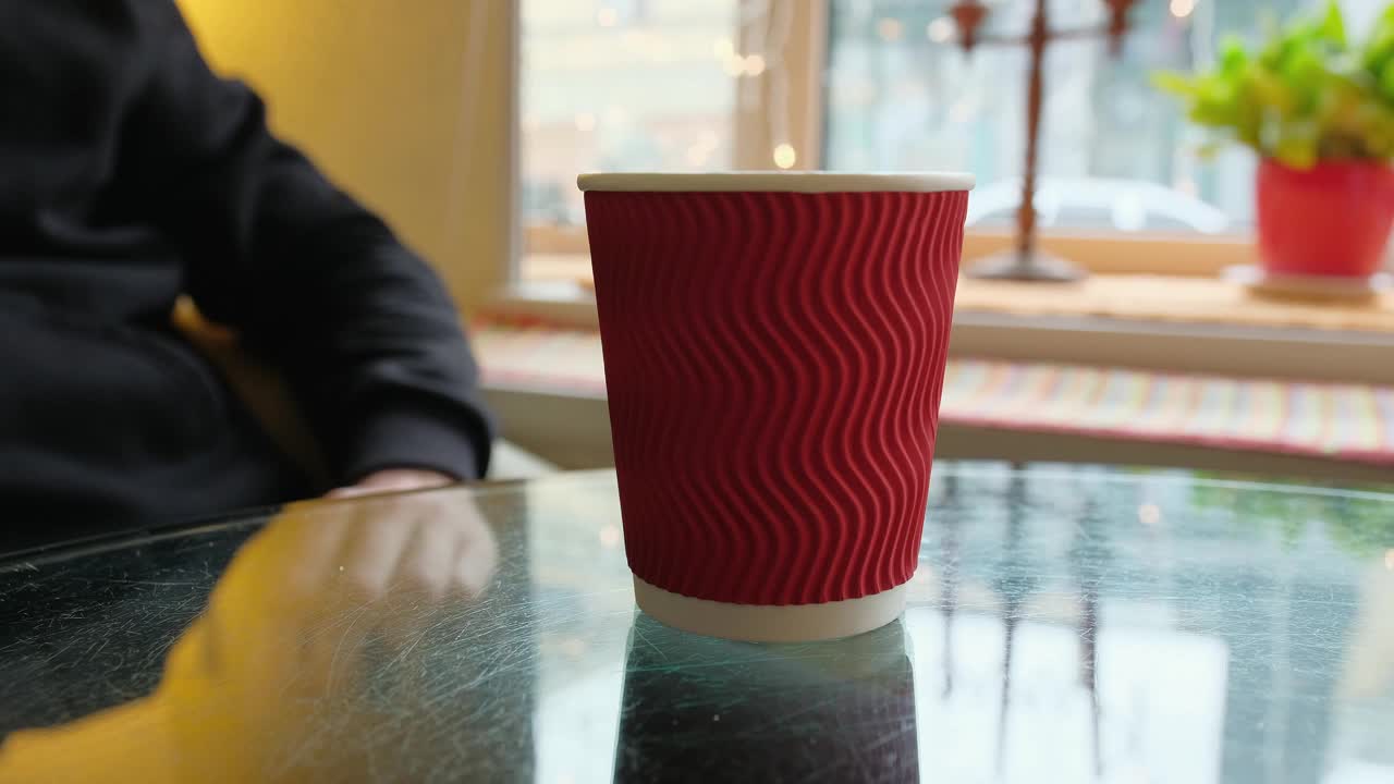 男性的手拿了一个纸杯咖啡在桌子上的咖啡馆。清晨，一名男子在咖啡馆里喝着芳香可口的咖啡视频下载