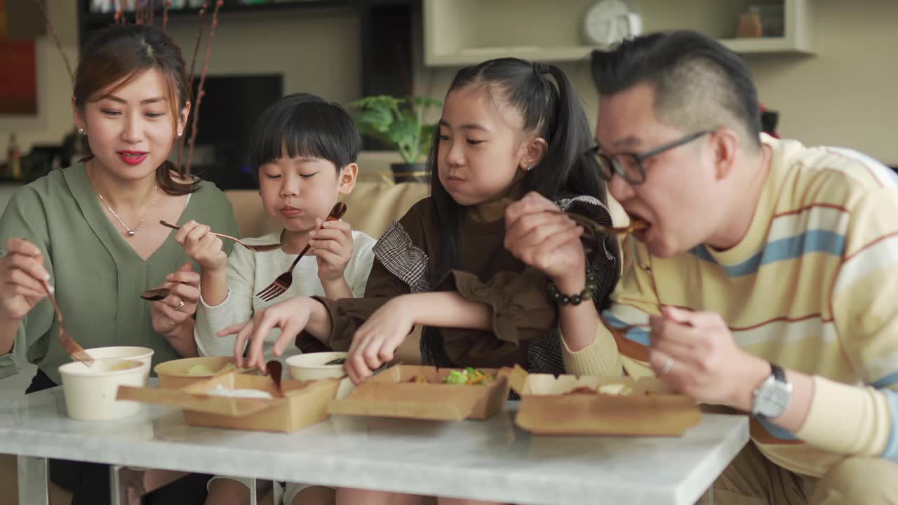 亚洲华人年轻家庭周末在客厅的电视前享受外卖食物视频下载