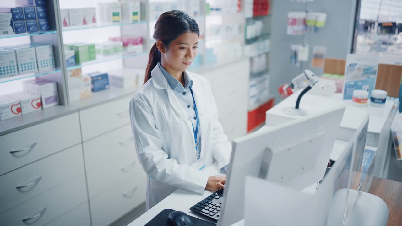 药店:美丽的亚洲药剂师使用结帐柜台电脑，做库存检查，在线处方药品包装，药物，维生素盒子，补充剂，保健产品视频素材