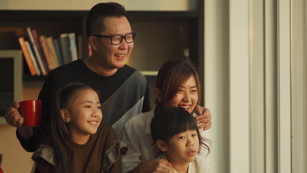 吉隆坡，一个中国家庭和两个孩子在客厅里透过窗户欣赏美丽的日落视频下载