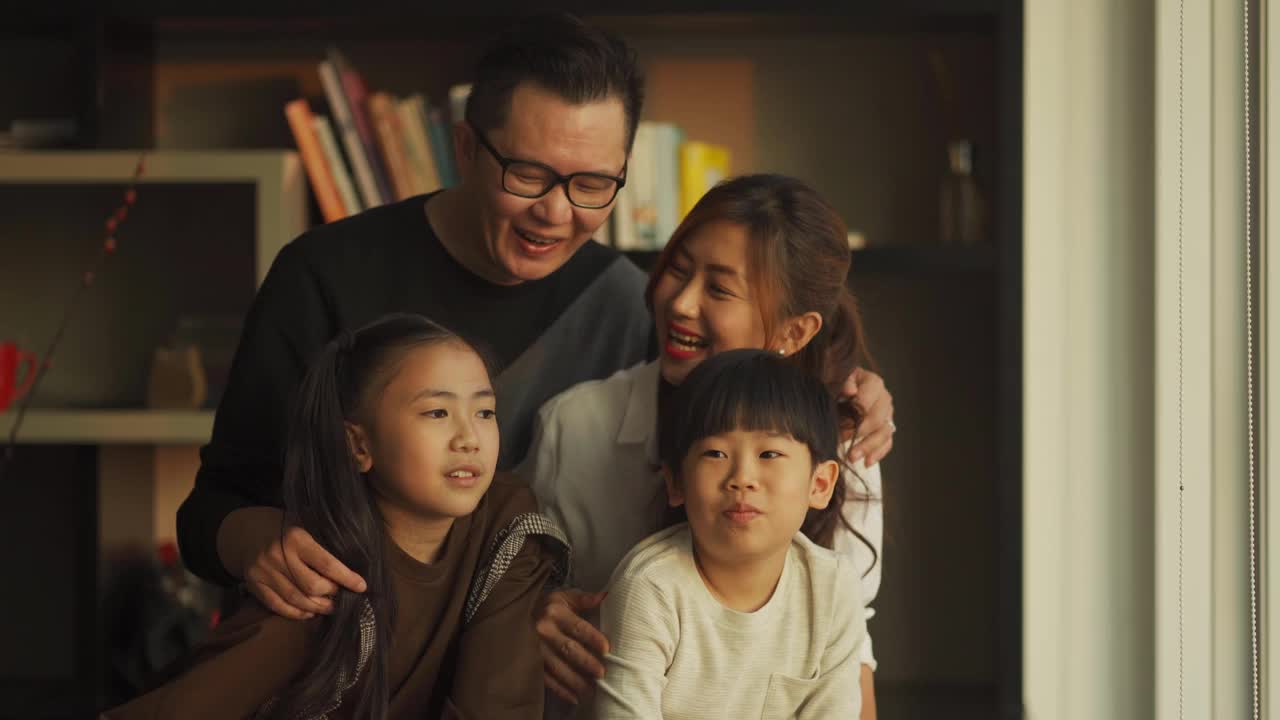 吉隆坡，一个中国家庭和两个孩子在客厅里透过窗户欣赏美丽的日落视频下载