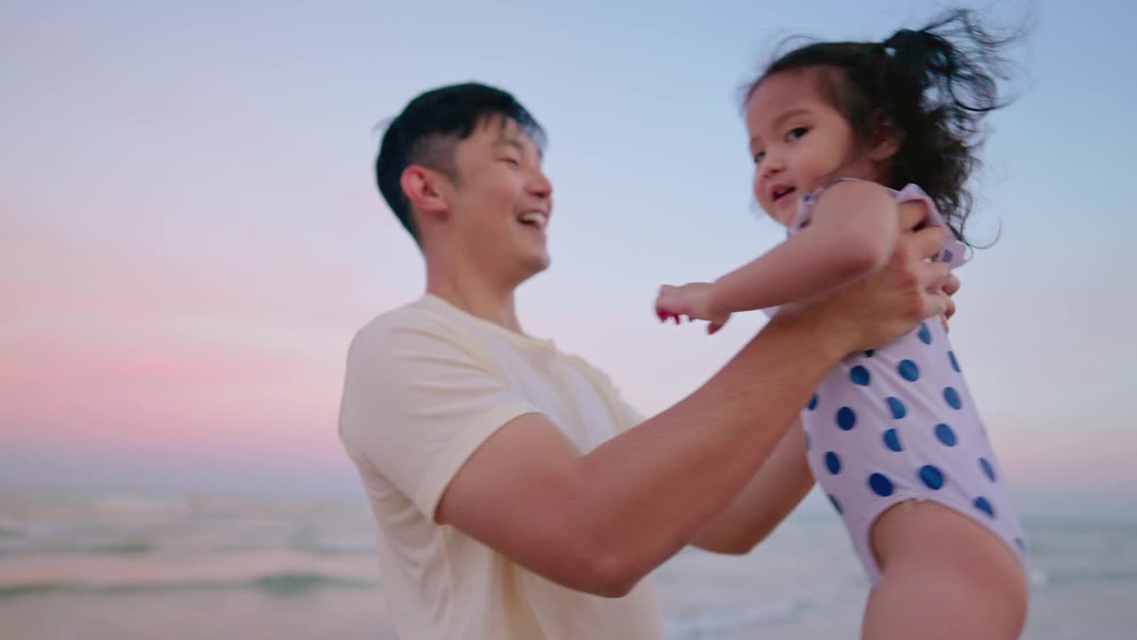 亚洲父亲抱着女儿在空中，而散步在海滩上的黄昏时间度假。视频素材